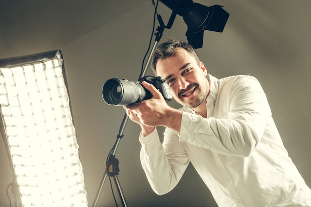 Homem novo considerável que prende uma câmera de DSLR.