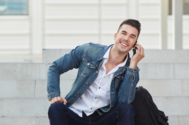 Homem novo considerável que sorri na chamada de telefone móvel fora