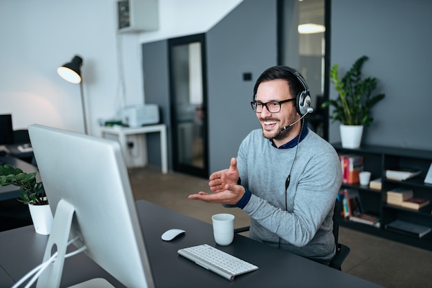 Homem novo considerável que tem a chamada em linha no escritório moderno.