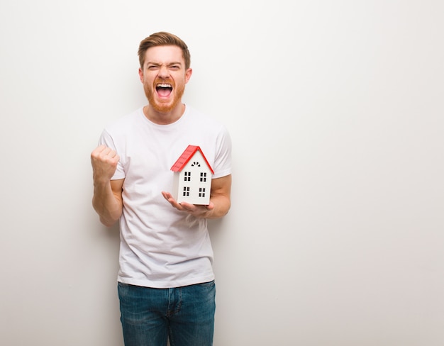 Homem novo do ruivo surpreendido e chocado. Segurando um modelo de casa.