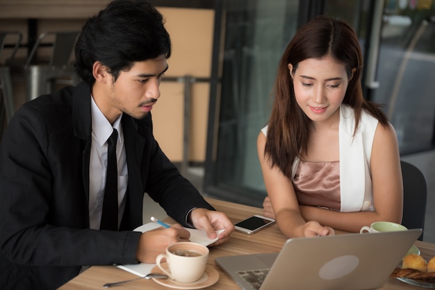 Homem novo e mulher asiáticos que procuraram dados no internet com o laptop no café.