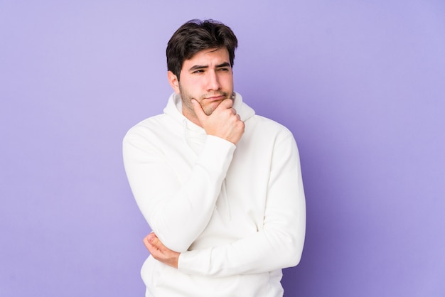 Homem novo isolado no roxo que olha lateralmente com expressão duvidosa e cética.