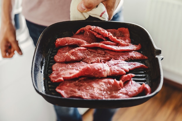 Homem novo que cozinha a carne na bandeja da grade em casa na cozinha. fechar-se.