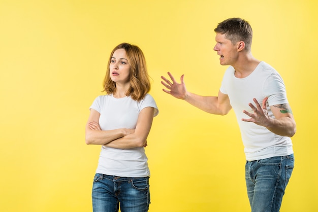 Homem novo que grita em uma amiga loura irritada que está de encontro ao fundo amarelo