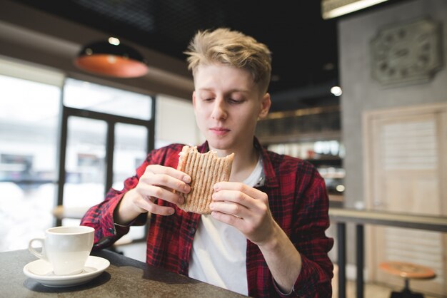 Homem novo que janta o sanduíche do panini no restaurante.