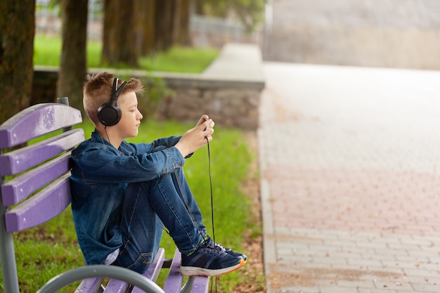 Homem novo que verifica seu telefone móvel ao ar livre. Adolescente em fones de ouvido usa seu smartphone.