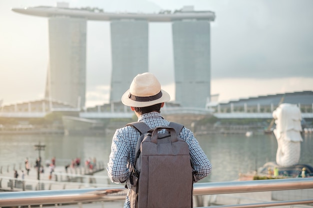 Homem novo que viaja com trouxa e chapéu na manhã, visita asiática de solo do viajante na baixa da cidade de Singapura. marco e popular para atracções turísticas. Conceito de viagens na Ásia