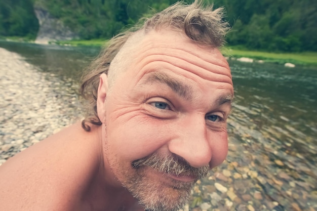 Homem nu louco com barba e moicano sorrindo no fundo de um rio de montanha