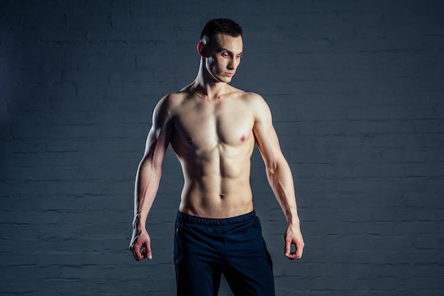 Homem nu sexy sem roupas demonstra os músculos abdominais em um fundo escuro.