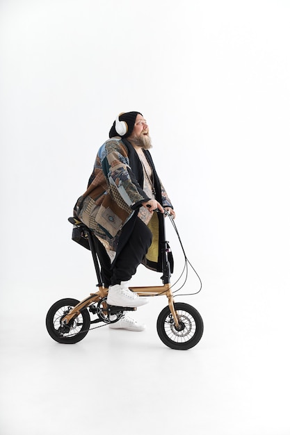 Homem obeso e tatuado de quimono segurando uma pequena bicicleta e sorrindo
