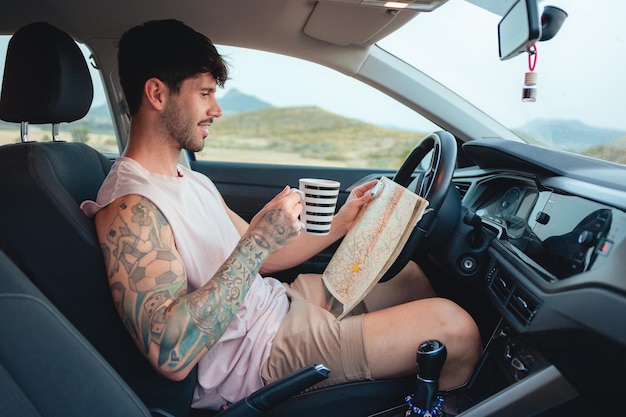 Homem olha para um mapa e bebe café dentro de um carro