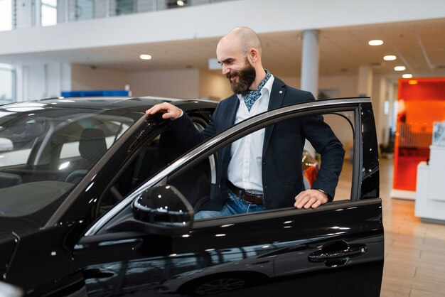 Homem olhando no interior do transporte na concessionária de automóveis. cliente em showroom de veículos novos, homem comprando automóvel, concessionária de automóveis