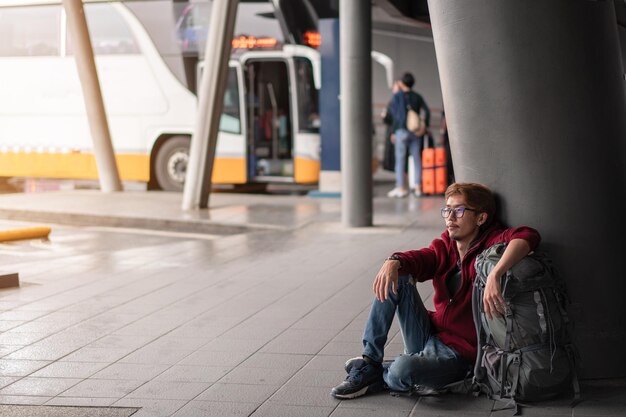 Foto homem olhando para longe enquanto está sentado no chão no ponto de ônibus