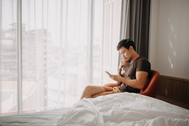 Homem olhando para o celular enquanto está sentado no quarto de hotel