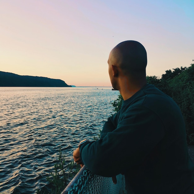 Homem olhando para o mar contra o céu claro durante o pôr-do-sol