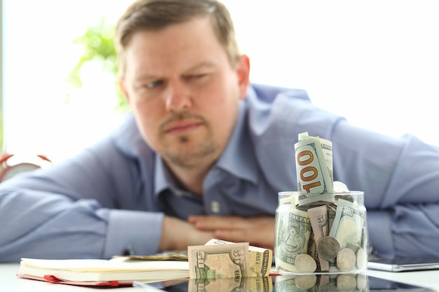 Foto homem olhando para o pote cheio de dinheiro pensando em suas dívidas