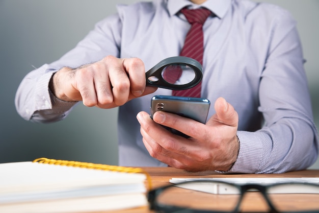 Homem olhando para o telefone com uma lupa.