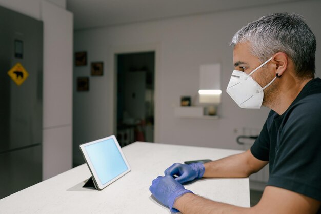 Foto homem olhando para um tablet com luvas e máscara covid19