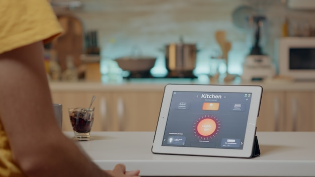 Homem olhando para um tablet com software de automação de iluminação sem fio colocado na mesa da cozinha, casa com sistema inteligente, acendendo as luzes. tablet digital com aplicativo de alta tecnologia que controla a eficiência elétrica