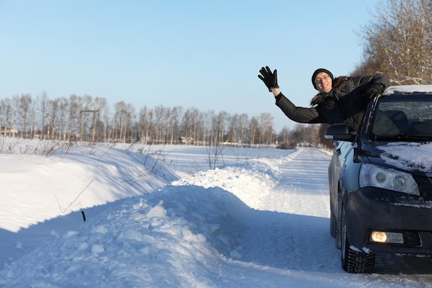 Homem olhando pela janela do carro para a estrada coberta de neve e sorrindo