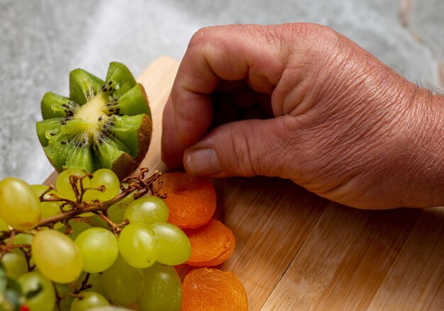 Homem organizando uma placa de frutas com uva verde, damasco, morango.