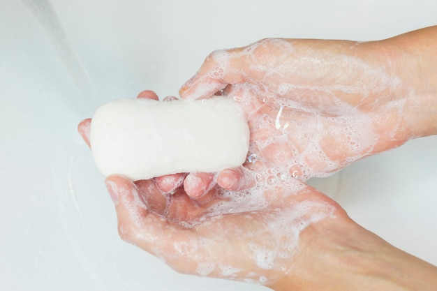 Foto homem ou mulher lavando as mãos, esfregando com sabão na pia debaixo de água.