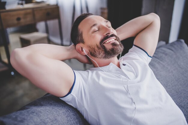 Foto homem ouvindo música em fones de ouvido e relaxando no sofá em casa