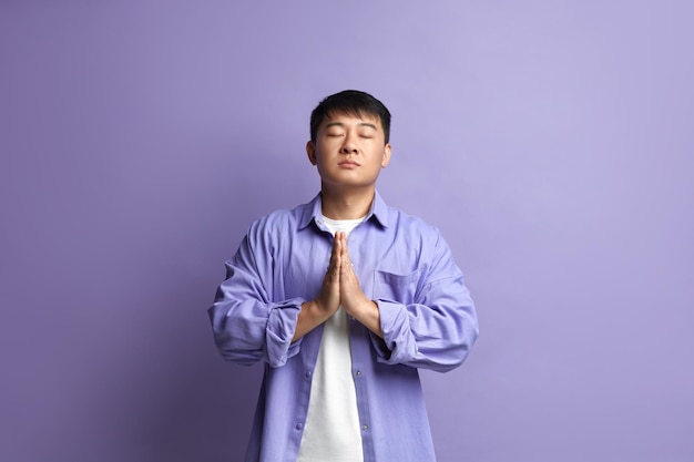 Foto homem pacífico meditando no retrato de estúdio de um cara asiático fazendo gesto de oração