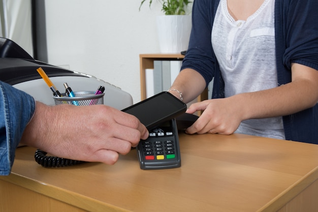 Homem pagando com tecnologia NFC no cartão de crédito com telefone, no restaurante, loja,