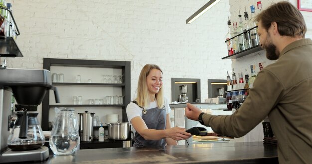 Homem pagando por café para viagem com tecnologia nfc da smartwatch sem contato no terminal em um café moderno. conceito de pagamento não em dinheiro.