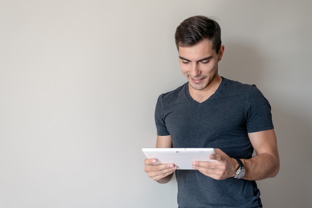 Homem para conceitual. jovem bonito usa um tablet em pé em uma parede cinza, copie o espaço