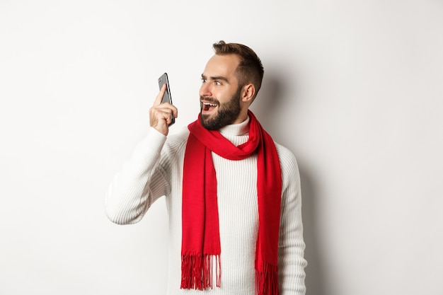 Homem parecendo confuso no celular depois de ouvir uma voz estranha, olhando para o smartphone chocado, de pé sobre um fundo branco