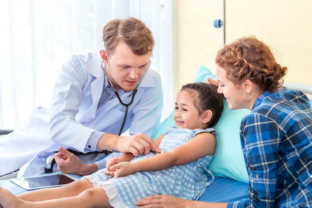 Homem pediatra (médico) examinando paciente menina usando um estetoscópio no hospital quarto.