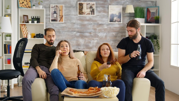 Homem pegando sua cerveja enquanto assiste tv com seus amigos no sofá. mulheres comendo pizza e batatas fritas.