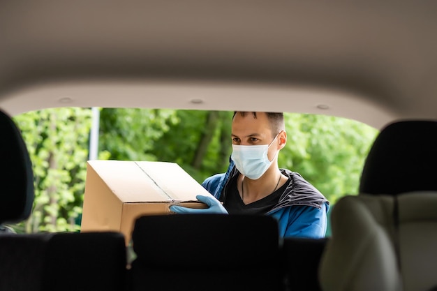 Homem pelo carro. Cara em um uniforme de entrega. Homem em uma máscara médica. Conceito de coronavírus.