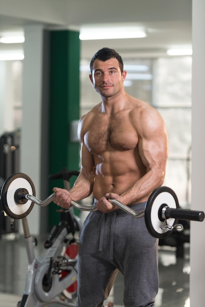 Homem peludo bonito malhando bíceps em uma academia de ginástica