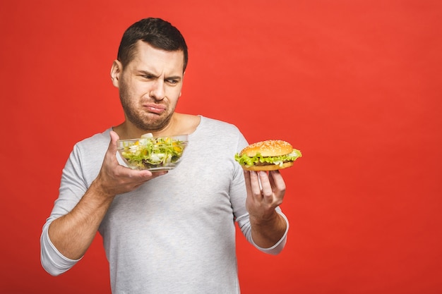 Homem pensando em escolher entre salada e hambúrguer, comida saudável e junk food