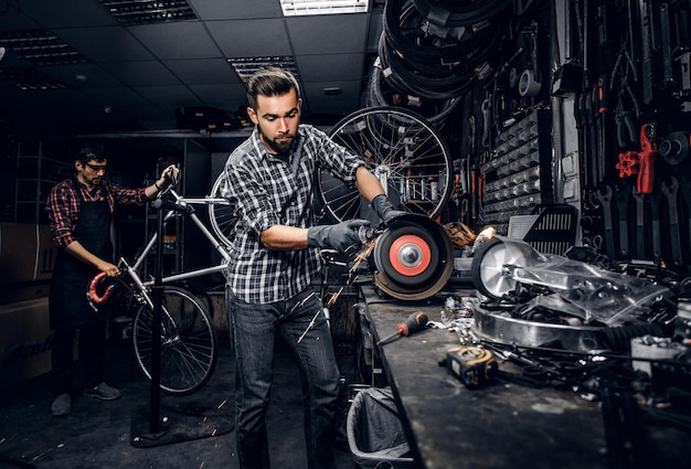 Homem pensativo atraente está trabalhando com máquina na oficina de bicicletas ocupada.