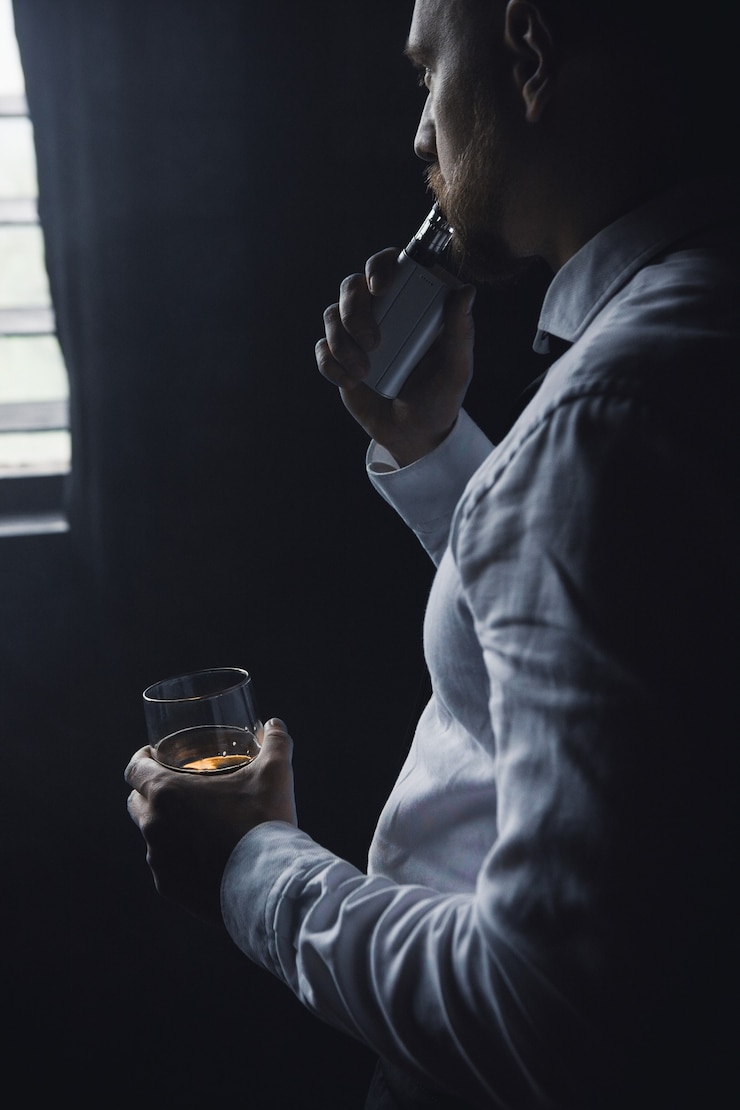 Homem pensativo e relaxante depois do trabalho. Homem de lazer com álcool e vapor em clube privado, maus hábitos. Vida luxuosa com whisky e fumo, fundo escuro