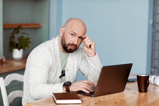 Homem pensativo está digitando em um laptop, trabalha em casa, trabalha on-line, coronavírus