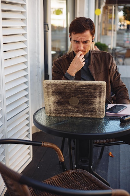 Homem pensativo sério navegando em laptop e trabalhando remotamente em projeto freelance