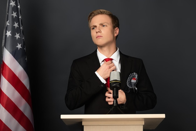 Foto homem pensativo tocando uma gravata na tribuna com bandeira americana em fundo preto