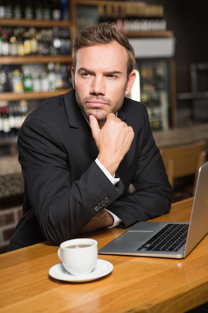 Homem pensativo usando laptop e tomando um café