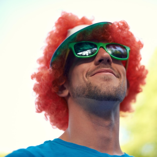 Homem peruca e óculos de sol com natureza céu e festival para diversão alegria e celebração pessoa verão e concerto com baixo ângulo sorriso e feliz para festa de evento ou sol para celebração e closeup