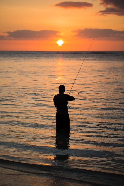 Homem pescando no Oceano Índico com a praia ao pôr do sol