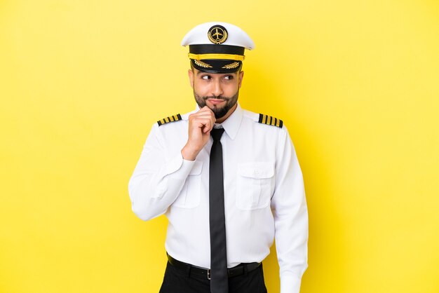 Homem piloto árabe de avião isolado em fundo amarelo, tendo dúvidas e pensando