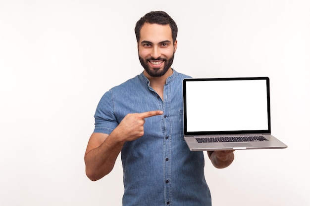 Foto homem positivo alegre apontando o dedo mostrando exibição vazia do blogueiro de laptop apresentando área de publicidade de espaço livre tiro de estúdio interno isolado no fundo branco