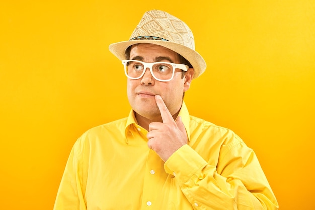 Homem positivo com chapéu panamá segurando o queixo pensa em dúvidas de férias toma decisão isolada no fundo amarelo do estúdio