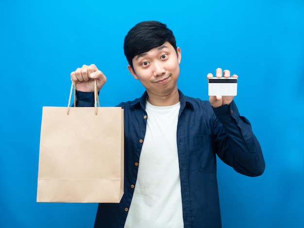 Homem positivo de retrato segurando saco de papel e cartão de crédito para compras de fundo azul