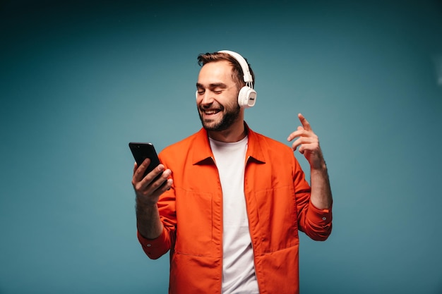 Homem positivo na jaqueta brilhante segurando smartphone e ouvindo música em fones de ouvido